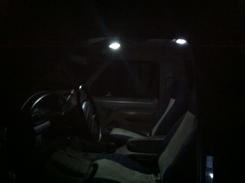 2004 Ford F-250 - The interior of a dark vehicle is illuminated by overhead dome lights. The view shows the steering wheel, dashboard, and seats.