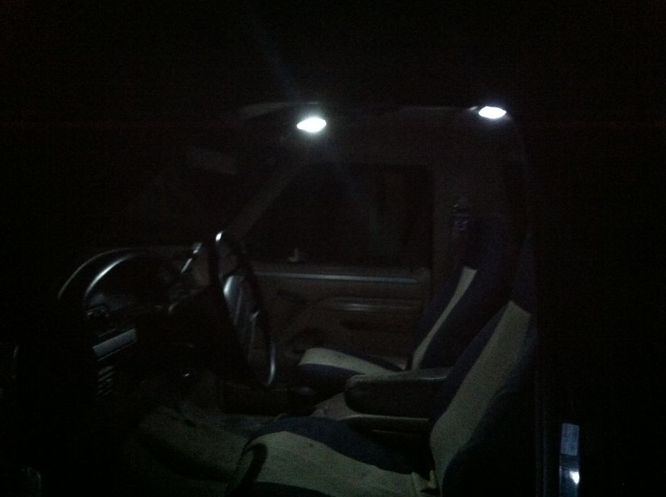 Interior of a vehicle at night, showing steering wheel, dashboard, and seats illuminated by dome lights.