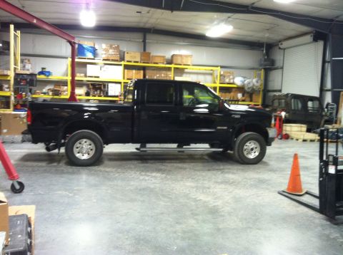 2004 Ford F-250 - A black, four-door Ford F-250 pickup truck is parked inside a warehouse. The truck is viewed from the side, showing its chrome wheels and s…