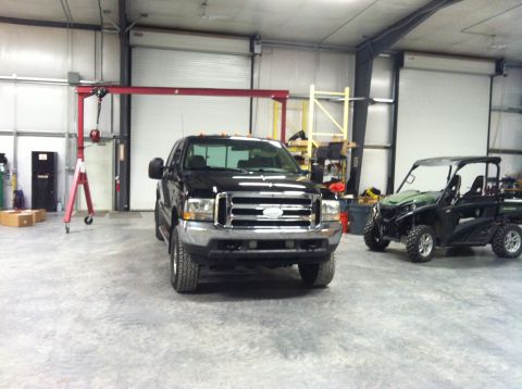 2004 Ford F-250 - A black Ford F-250 pickup truck is parked inside a garage next to a green and black UTV. A red gantry crane is positioned to the left of th…