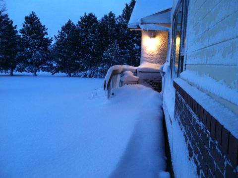 2004 Ford F-250 - A snow-covered yard and the side of a house with a porch light on. Tall evergreen trees are visible in the background.