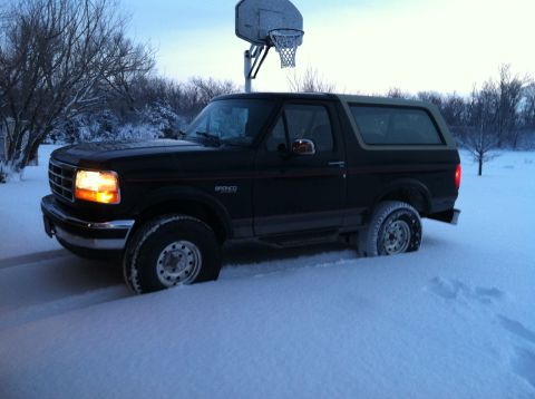 2004 Ford F-250 - A black Ford Bronco is parked in deep snow with its front headlight illuminated. A basketball hoop stands behind the vehicle against a pale…
