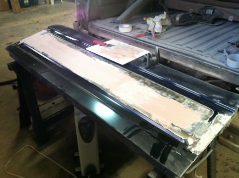 2004 Ford F-250 - A black truck tailgate is being repaired and sanded on sawhorses. Body filler is applied and being smoothed, with tools and tape visible in…