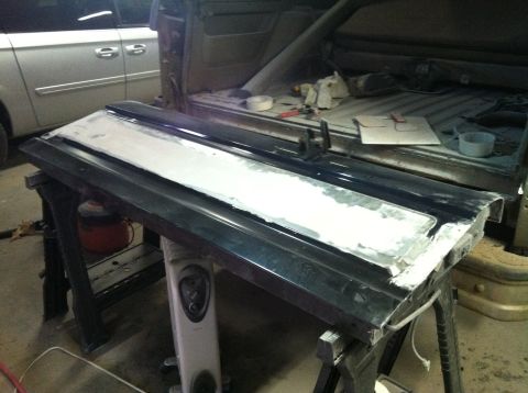 2004 Ford F-250 - A dark-colored truck tailgate is propped up on sawhorses and appears to be undergoing bodywork, with white filler applied to a section of i…