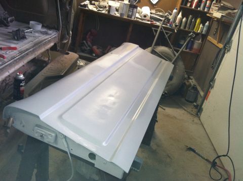 2004 Ford F-250 - A white painted tailgate is propped up on a stand in a garage. The tailgate is the primary focus, with a workbench and shelves filled with…