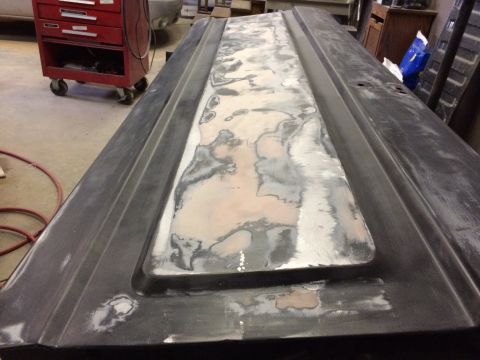 2004 Ford F-250 - A dark-colored truck door panel is undergoing bodywork, with areas of primer and filler visible. The panel is lying flat in what appears to…