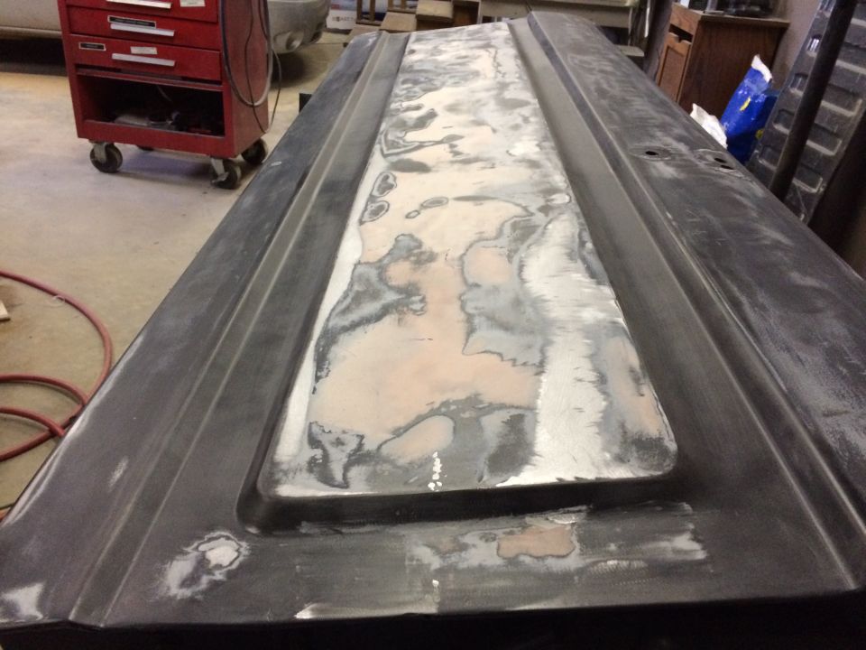 Dark truck door panel with body filler and primer, in a workshop.