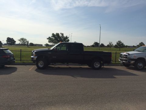 2004 Ford F-250 - A black Ford F-250 pickup truck is parked in a lot next to a silver Dodge Ram pickup truck. The trucks are parked on asphalt with a black m…