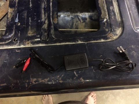 2004 Ford F-250 - A black Audi battery charger with alligator clips and a power cord is laid out on a dark, weathered surface. The background shows the ruste…
