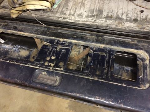 2004 Ford F-250 - The inner workings of a dark blue tailgate are visible, showing rusty latches and mechanisms. A yellow strap is coiled in the upper left co…