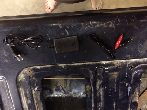 2004 Ford F-250 - A black Audi battery charger with red and black alligator clips is laid out on a dark blue, weathered surface. The charger has the Audi rin…