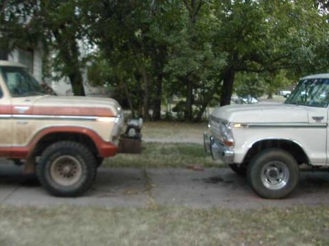 1979 Ford Bronco - A pair of classic Ford Broncos are parked side-by-side on a lot with trees in the background.