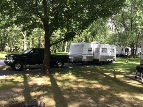 2004 Ford F-250 - A black Ford F-250 pickup truck is parked next to a travel trailer at a campsite. The truck is positioned under the shade of a large tree.