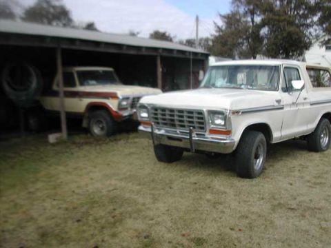1979 Ford Bronco - A white 1979 Ford Bronco is parked in front of a covered area, with another vintage Bronco visible behind it.
