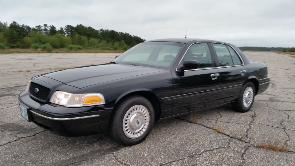 Black Ford Crown Victoria sedan front three-quarter view on cracked pavement