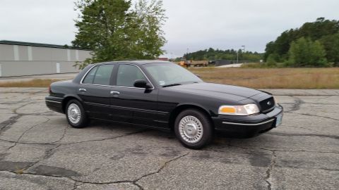 2001 Ford Crown Victoria - A black 2001 Ford Crown Victoria is parked outdoors on a cloudy day, with a building and trees in the background.