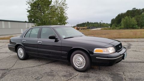 2001 Ford Crown Victoria - A black 2001 Ford Crown Victoria sedan is parked on cracked asphalt under an overcast sky.