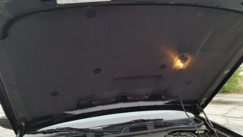 Car hood is open, showing the underside insulation and a small light. Wipers and part of the engine bay are visible below