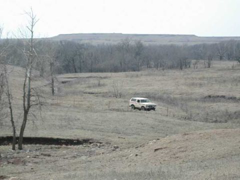 1979 Ford Bronco - A 1979 Ford Bronco navigates a rural, open landscape under a hazy sky.