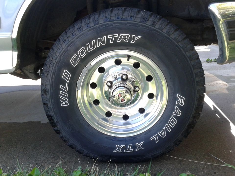 Close-up of a chrome wheel with a "Wild Country Radial XTX" tire. Center cap has a red and black logo