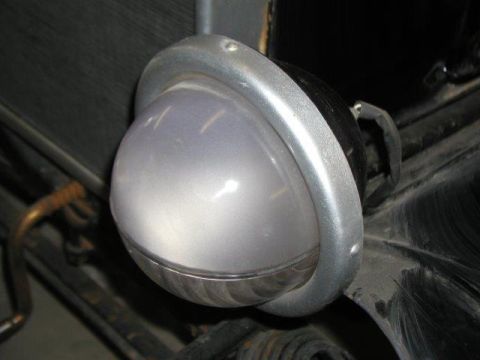 1923 Ford Model T - Close-up of a vehicle headlight with a silver bezel and a frosted glass lens. Text at bottom reads 'SUPERMOTORS.NET'.