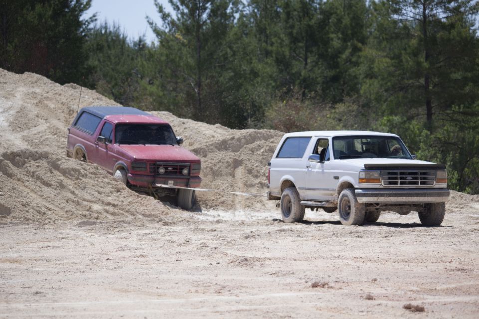 1995 Ford Bronco pulling a stuck red Ford Bronco out of sand