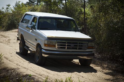 1995 Ford Bronco - A white 1995 Ford Bronco navigates a sandy track surrounded by dense foliage.