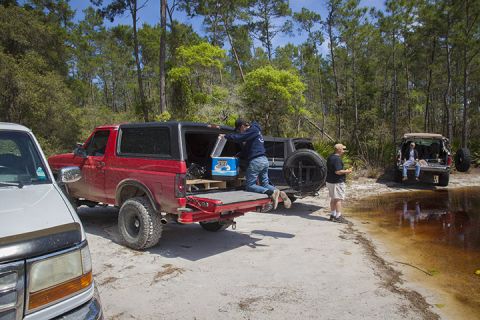 1995 Ford Bronco - People are loading gear into a red Ford Bronco parked near a body of water with trees in the background.