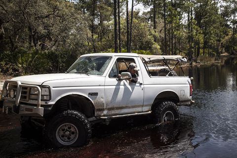 1995 Ford Bronco - A white Ford Bronco navigates through a watery terrain surrounded by trees.