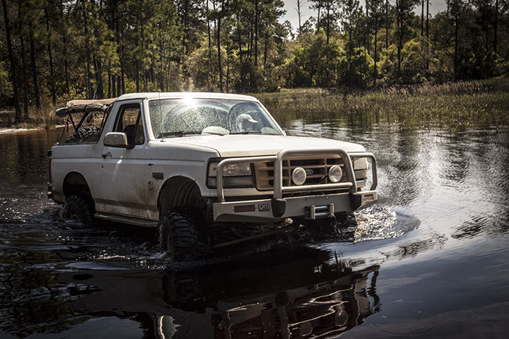 White 1995 Ford Bronco driving through water with a brush guard