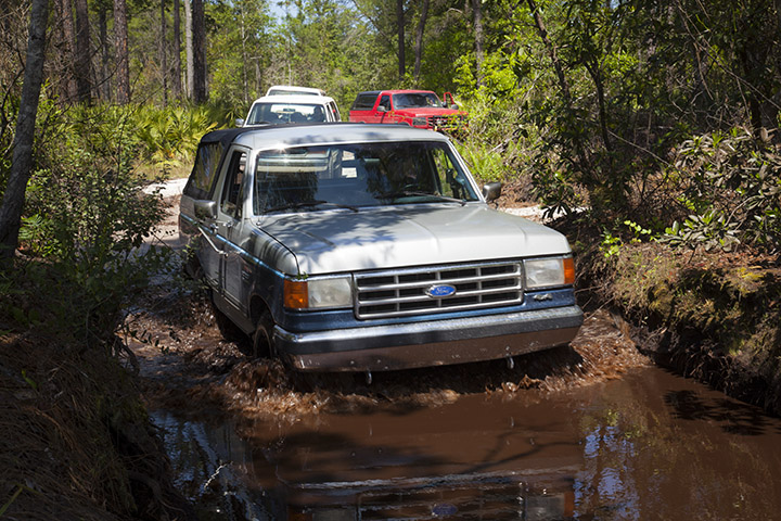 Ford Bronco driving through a muddy trail with other vehicles behind it