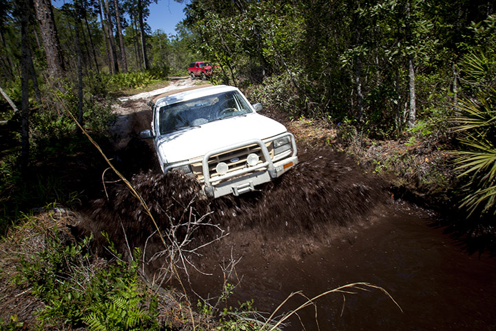 White 1995 Ford Bronco splashing through mud on a trail