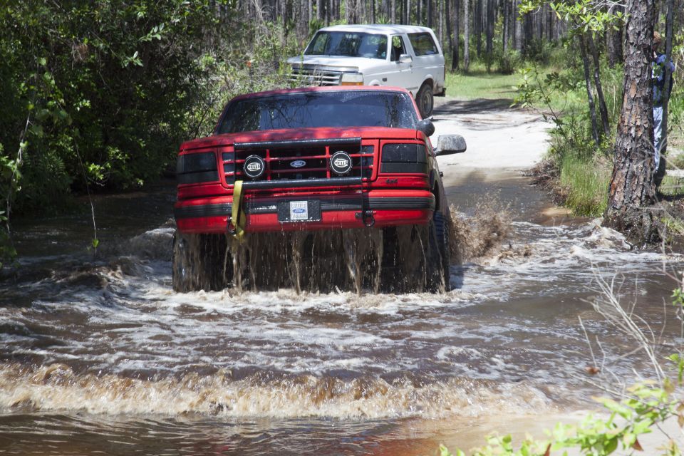 Red Ford Bronco driving through water, white Ford Bronco behind it