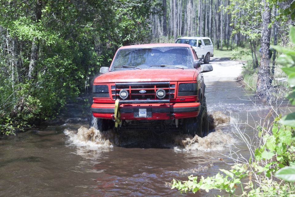 Red 1995 Ford Bronco driving through water, front view