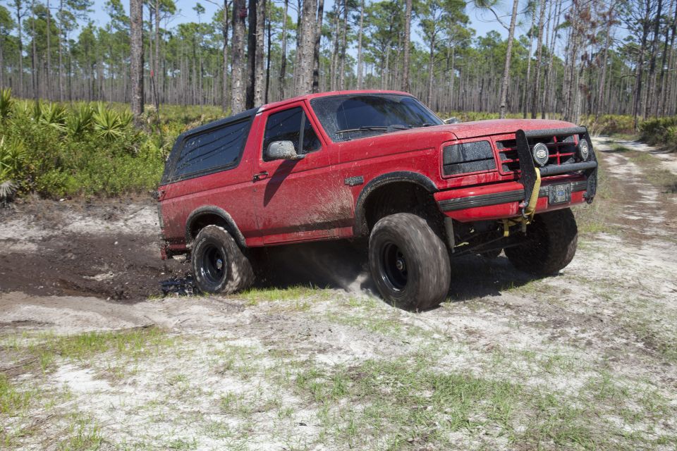 Red Ford Bronco driving through mud and sand in a wooded area