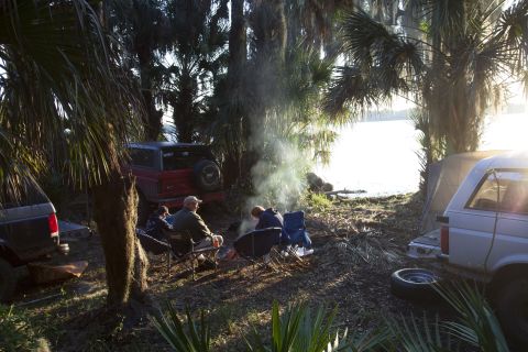 1995 Ford Bronco - Campfire scene with a 1995 Ford Bronco and another SUV, set by a lake with palm trees.