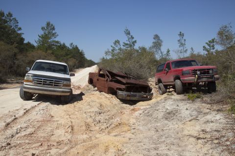 1995 Ford Bronco - Three vehicles navigate a challenging dirt road with sandy inclines and rough terrain.