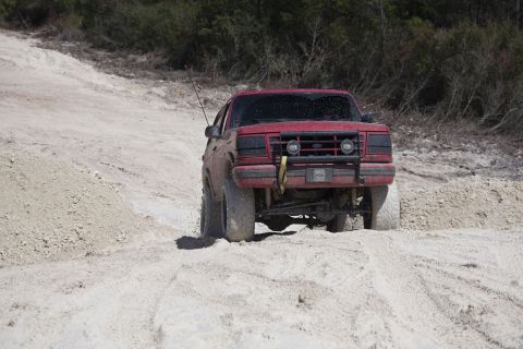 1995 Ford Bronco - Red 1995 Ford Bronco navigates a dirt path with large tires.