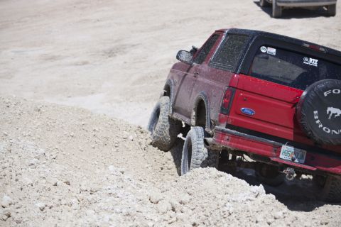 1995 Ford Bronco - A red Ford Bronco navigates a sandy incline, its tires digging into the loose terrain.