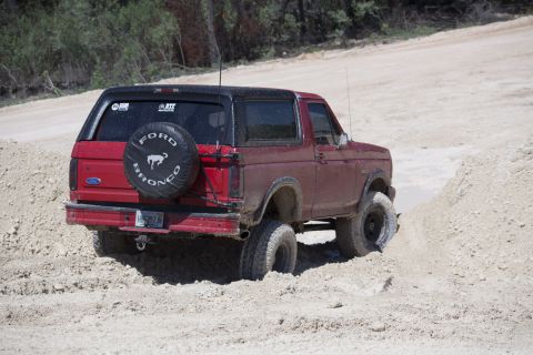 1995 Ford Bronco - A red Ford Bronco navigates a sandy terrain, its rear tire visible as it gets stuck.