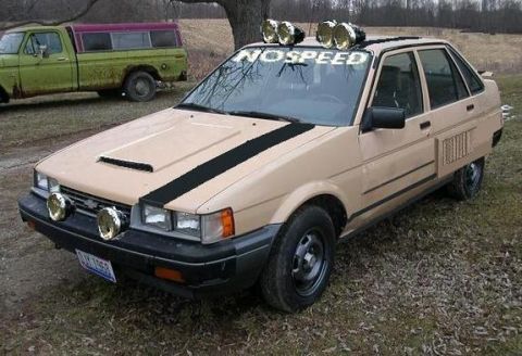2000 Mercury Grand Marquis - A modified tan sedan with extra lights and a roof-mounted light bar is parked outdoors next to a vintage pickup truck.