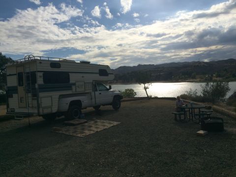 1997 Dodge 3500 - A white truck camper is parked at a campsite next to a lake with mountains in the background.