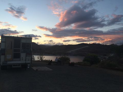 1997 Dodge 3500 - A camper van is parked near a lake as the sun sets, casting colorful hues across the sky.