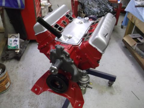 1957 Ford Custom Sedan - A red V8 engine with silver valve covers is mounted on a red engine stand in a workshop.