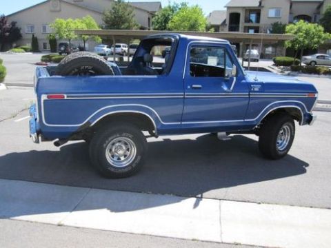 1978 Ford Bronco - A blue 1978 Ford Bronco is seen from the side, parked in a lot with buildings in the background.
