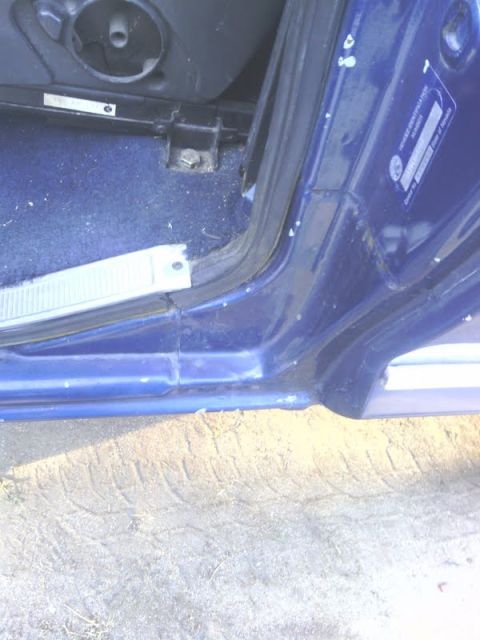 1978 Ford Bronco - Close-up view of the interior door jamb and floor of a blue vehicle, showing a VIN sticker and tire tracks on the ground outside.