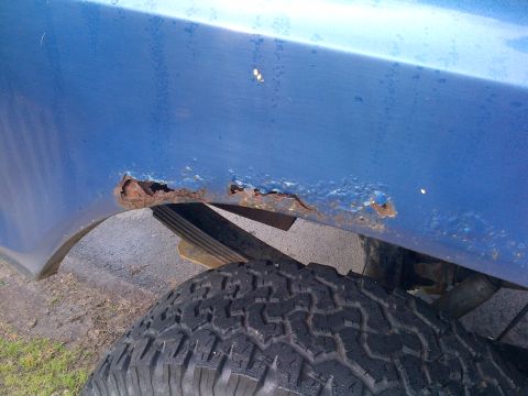 1978 Ford Bronco - Rust has heavily corroded the rear wheel well of this blue vehicle, obscuring any specific year identification.