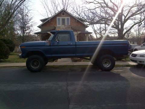 1978 Ford Bronco - A blue pickup truck is parked on the side of the road in front of a house.