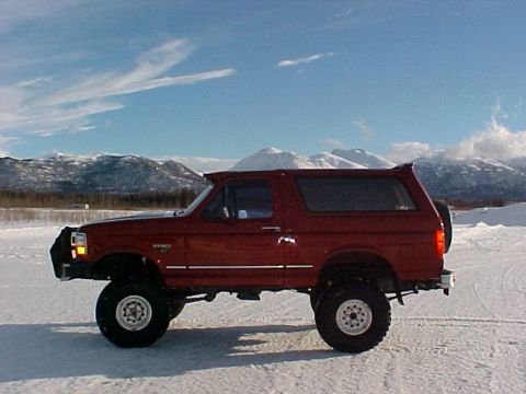1995 Ford Bronco - This red Ford Bronco SUV is shown from the side in a snowy, mountainous environment.