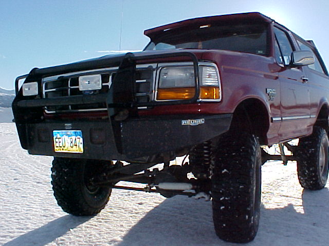 Lifted dark red Ford Bronco with brush guard on white salt flat, front 3/4 view